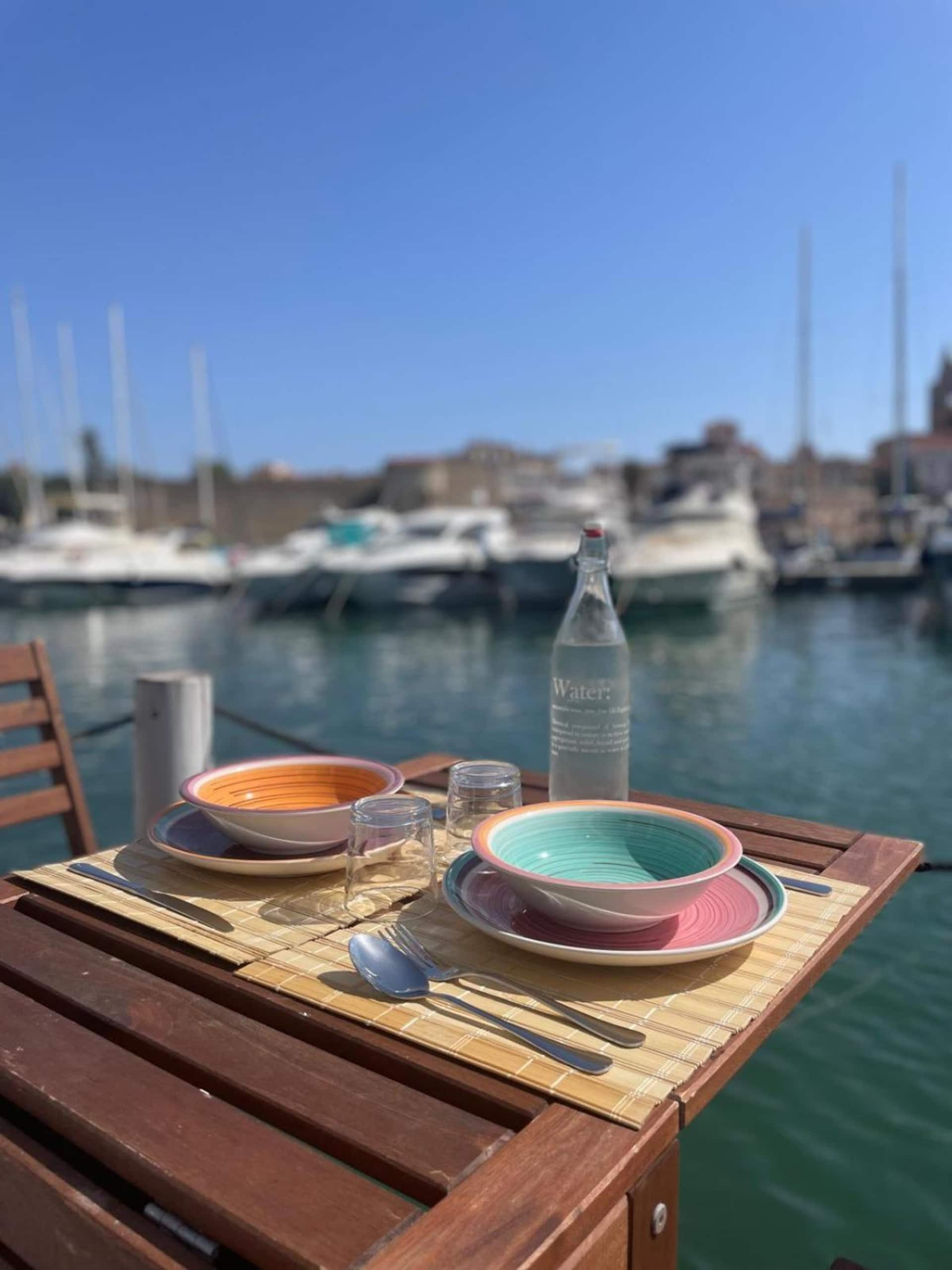 Tavolo apparecchiato sul ponte con ceramiche colorate e il porto sullo sfondo